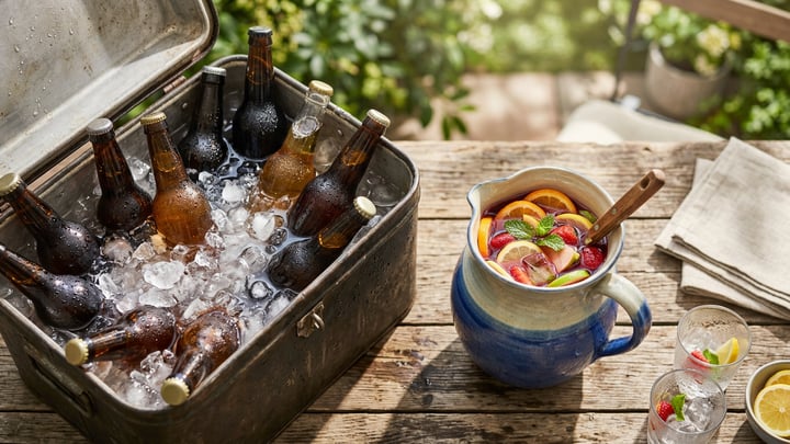 Open cooler with ice, water and bottles, and a jug of fruit punch beside it on a summer table