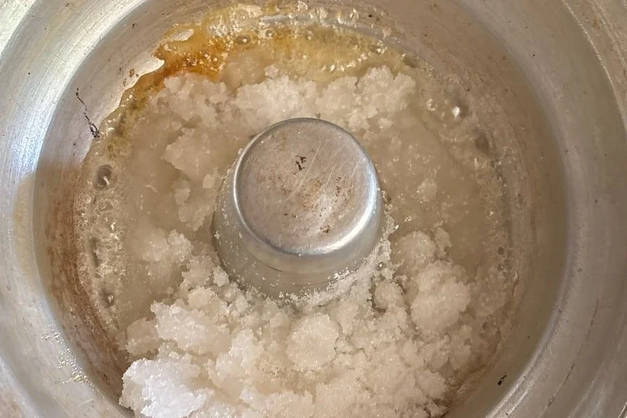 Uopløste hvide sukkerklumper i sirup i en metalform, hvor kanten allerede har taget farve